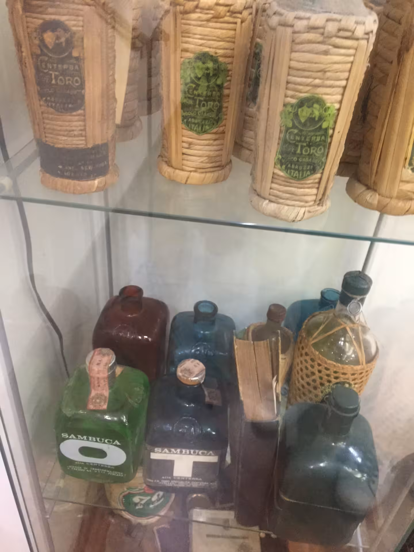 Collezione di bottiglie storiche e sambuca in vetrina alla distilleria Toro durante visita guidata e degustazione