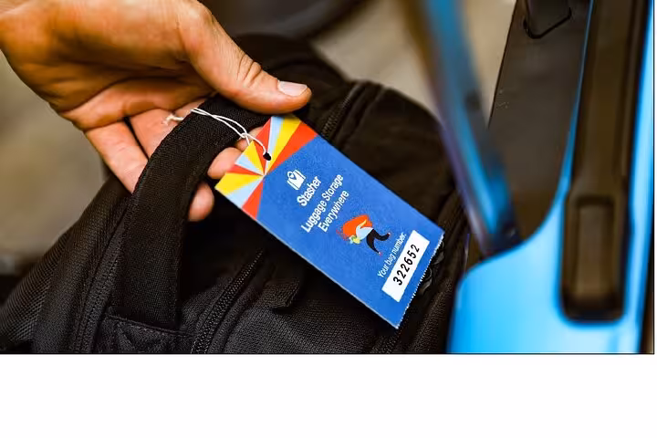 Hand attaching tag to backpack beside suitcase for secure Toronto luggage storage and same-day bag drop service