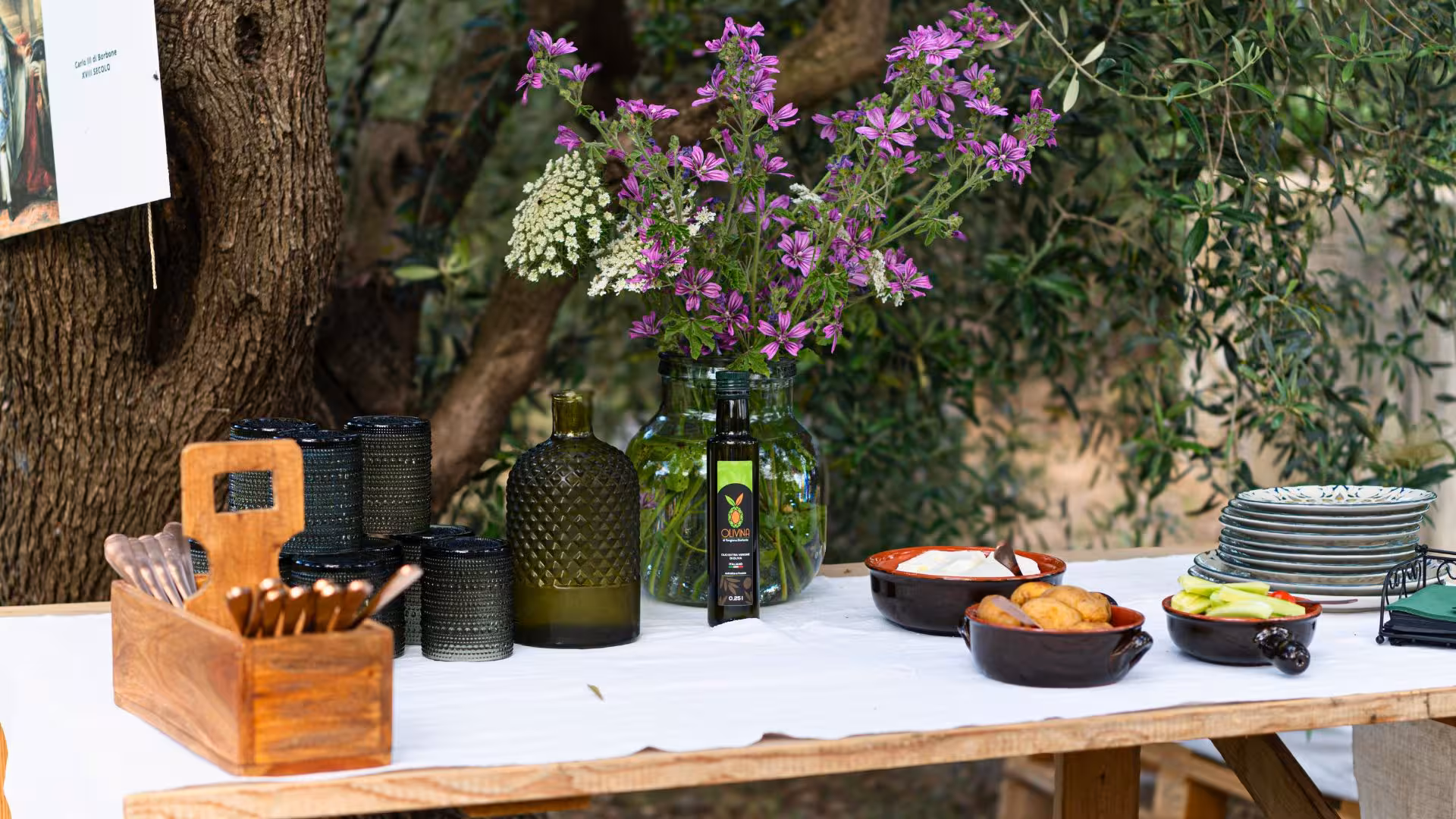 Rustic table setup with olive oil, flowers, and snacks for tasting session in Lotzorai during Tortolì oil mill visit.