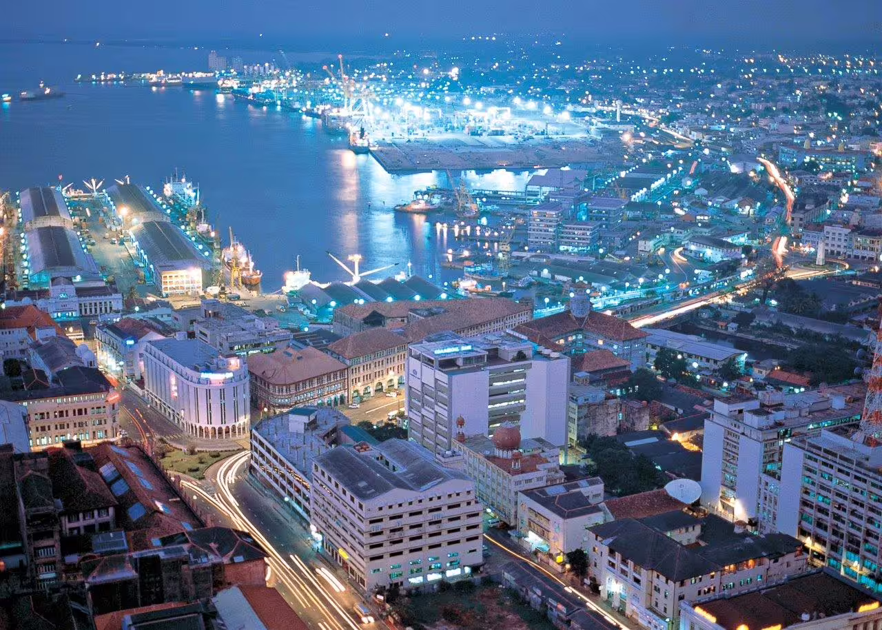 Vibrant cityscape of a bustling coastal city at night, showcasing illuminated buildings and lively harbor.