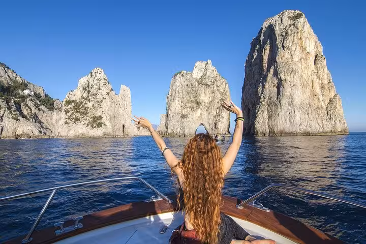 A tourist on a boat admires the iconic Faraglioni rock formations during a Capri excursion from Sorrento.