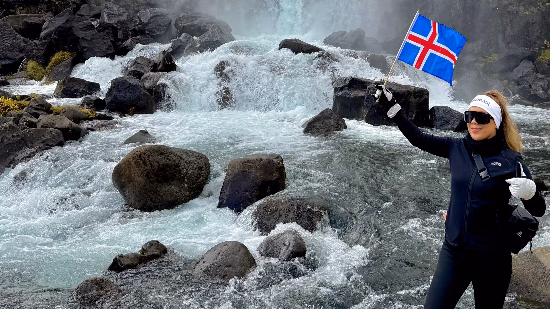 Tourist holding Icelandic flag in front of a stunning waterfall on a Golden Circle private tour.