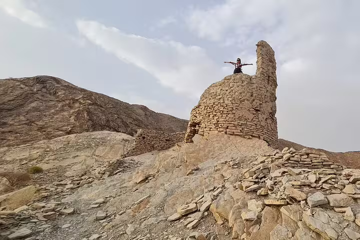 Tourist stands atop ancient stone ruins in Jebel Akhdar, offering breathtaking views of the rugged landscape.