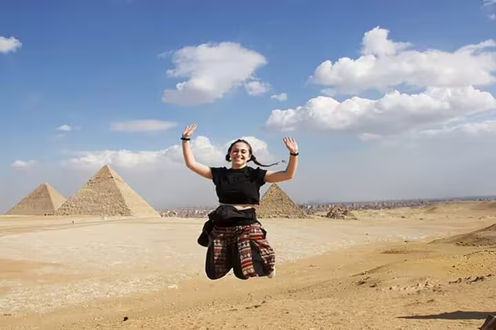 Tourist jumping with Giza Pyramids in background, highlighting a 2-day Ancient Egypt tour with pyramids and museums