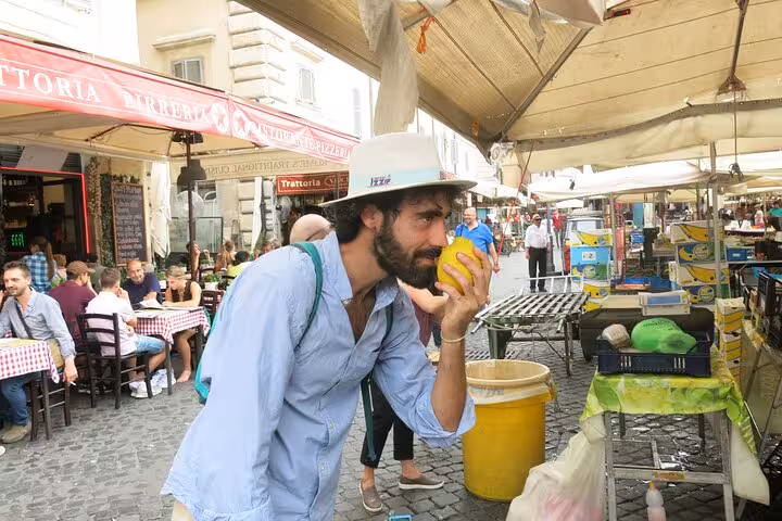 Tourist savoring the aroma of a lemon at a vibrant local market in Rome on a vegetarian food tour.