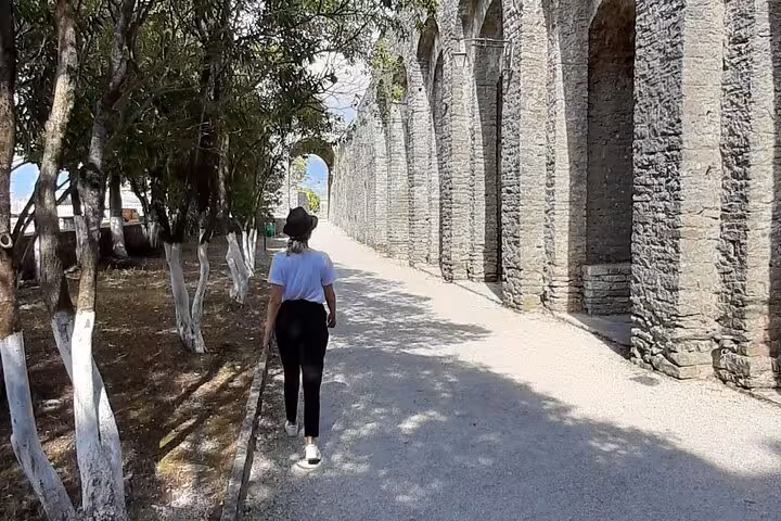 Tourist walking along historic stone arches in Albania, showcasing the ancient architecture and lush surroundings.