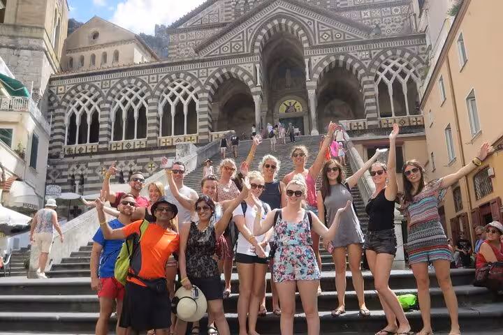 Group of tourists celebrating on the steps of Amalfi Cathedral, showcasing stunning architectural details.
