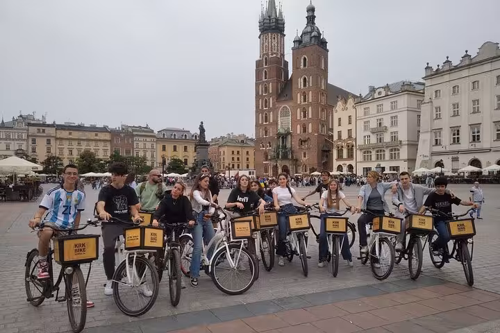 Tourists on bikes explore the historic Jewish Quarter, pausing in front of a grand cathedral during the tour.