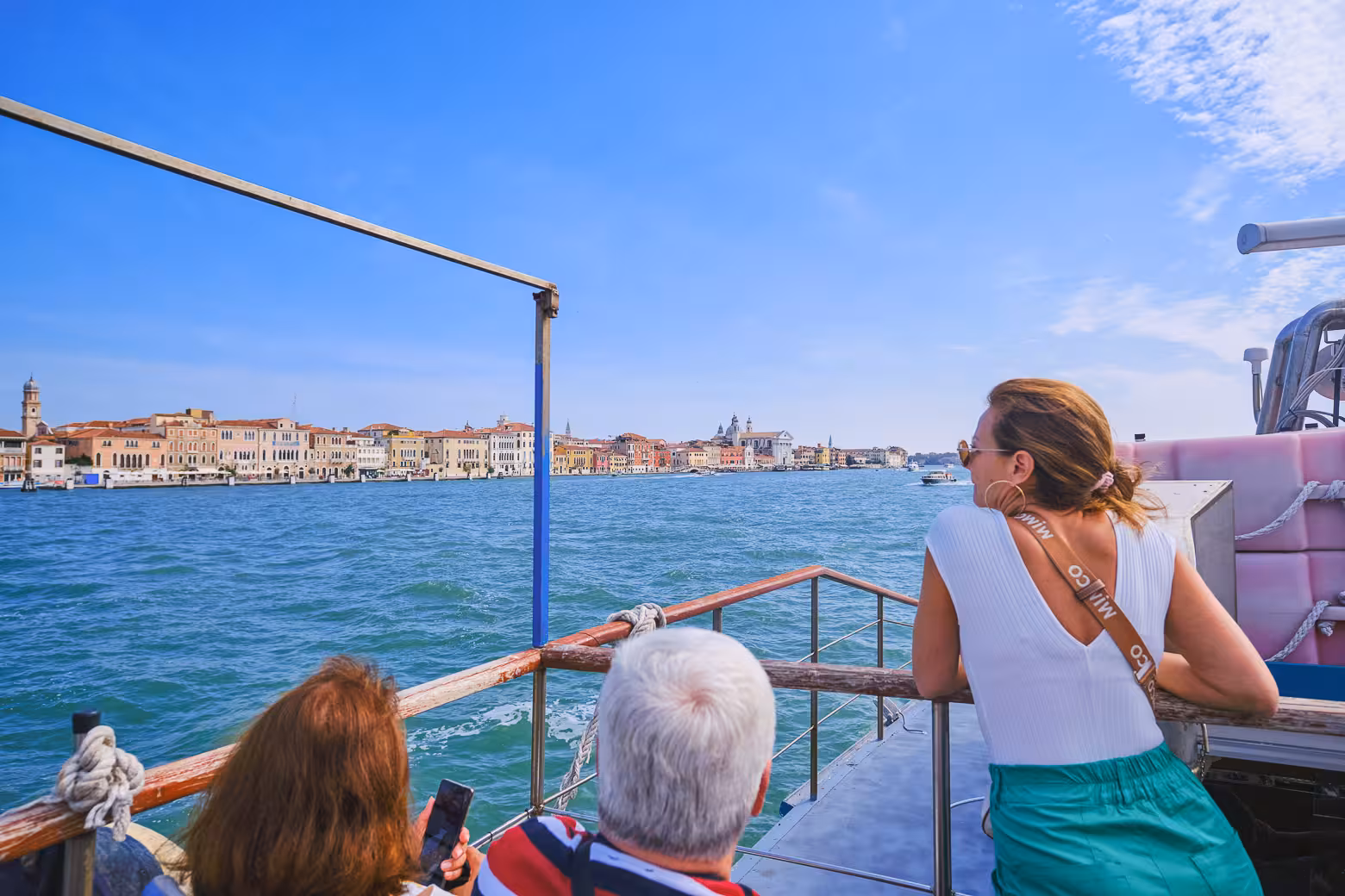 Tourists enjoy a scenic boat ride towards Venice, capturing the vibrant cityscape under a clear blue sky.