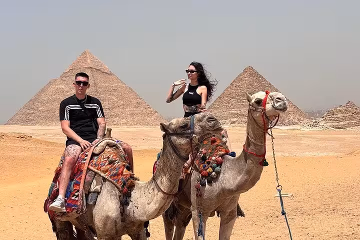 Tourists on camel ride in Giza Desert with Great Pyramids backdrop, private Giza pyramids and Sphinx tour