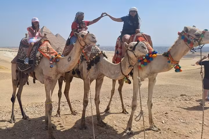 Tourists riding camels at the pyramids in Egypt, experiencing a private tour with camel rides and local insights.