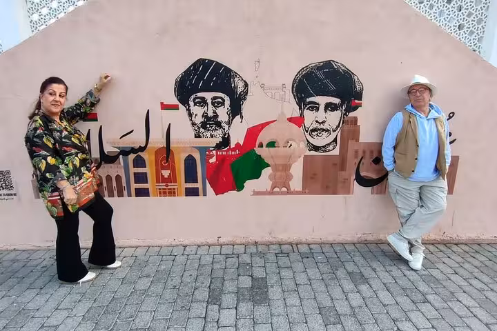 Tourists posing by colorful mural in Nizwa, discovering Omani culture and street art on a private evening sightseeing trip