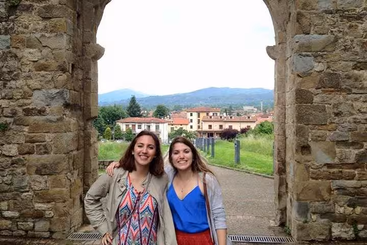 Two tourists smiling under an ancient stone archway in Cortona with scenic views of the Tuscan landscape.