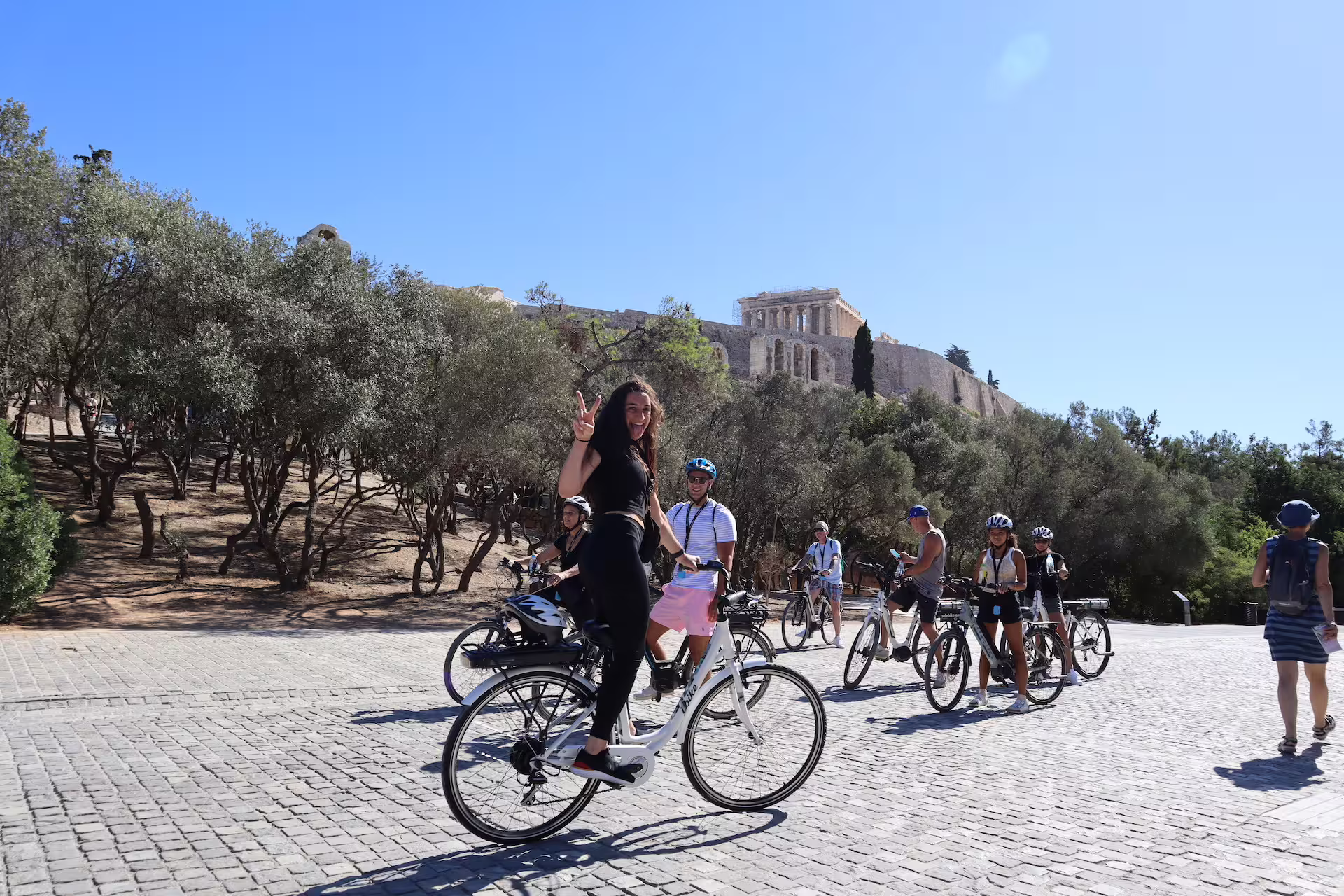 Group of tourists on e-bikes exploring the historic Acropolis area in Athens under a clear blue sky.