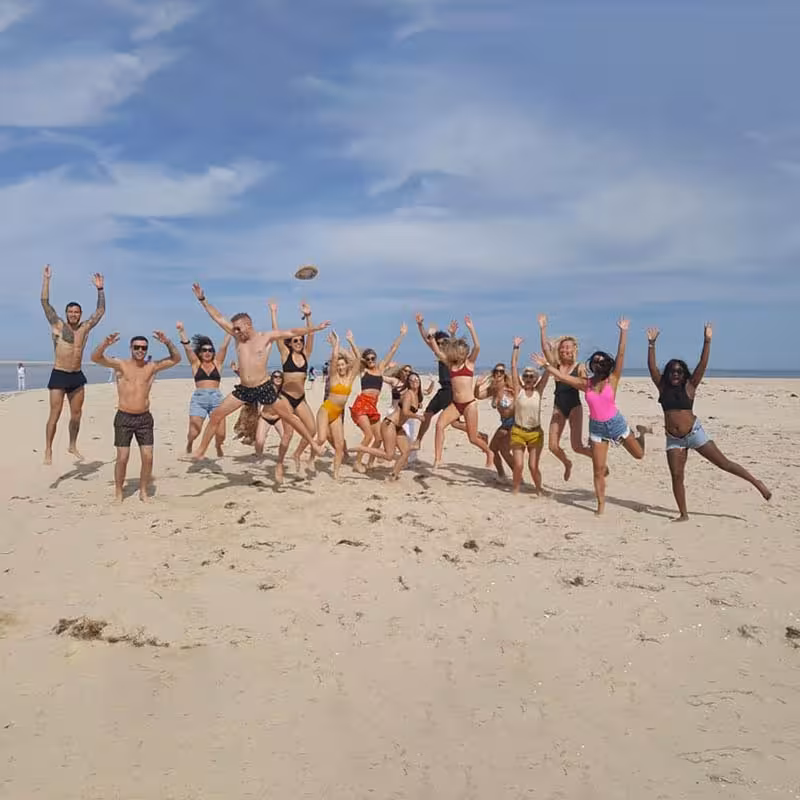 Excited group of tourists jumping on a pristine sandy beach during a visit to Culatra Island.