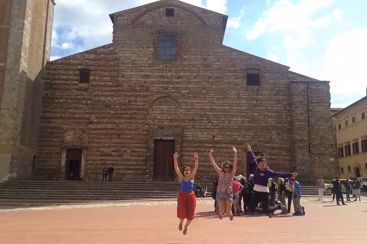 Tourists joyfully jumping in front of the historic church in Montepulciano, capturing the vibrant atmosphere of the tour.