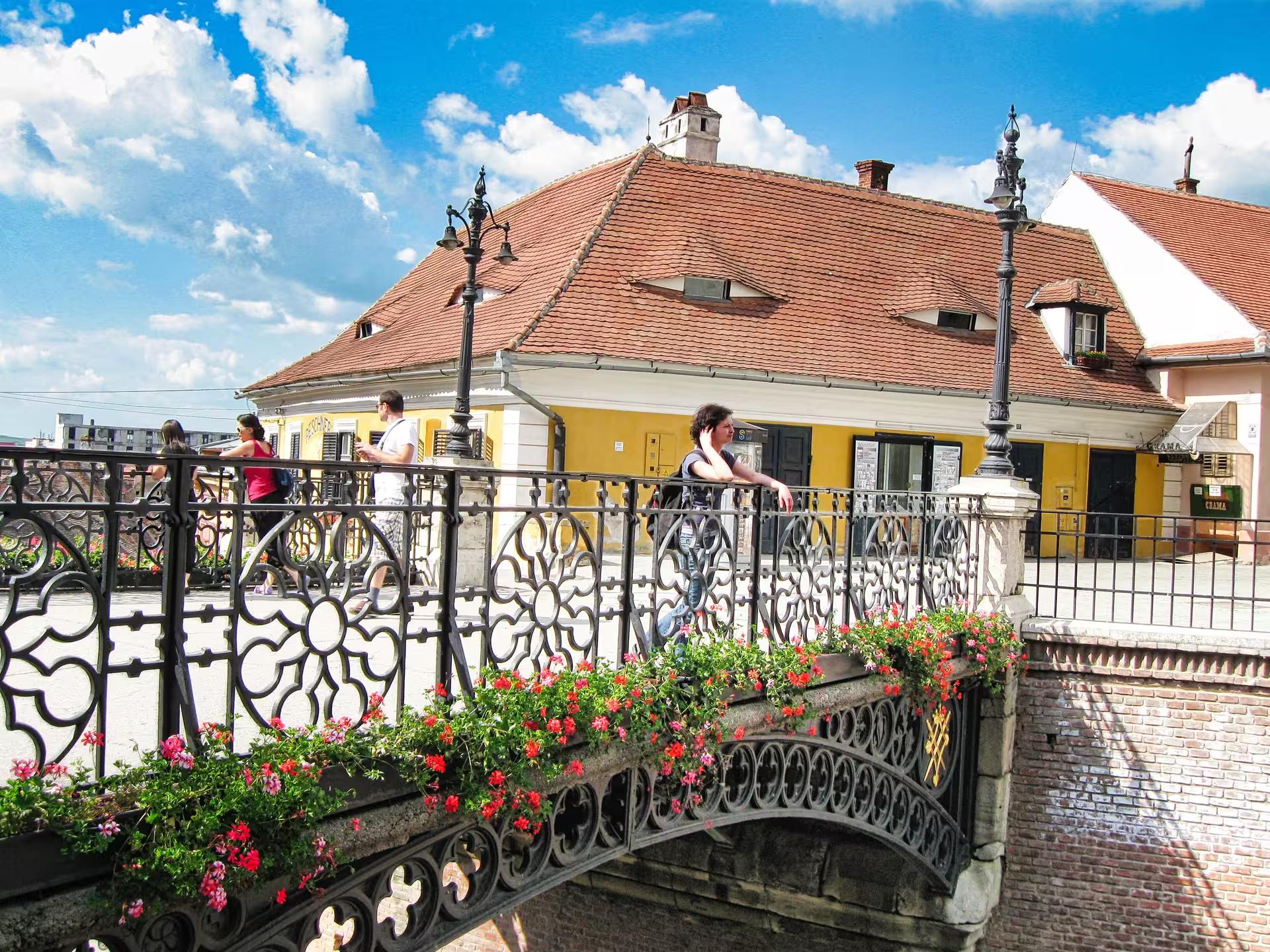 Tourists crossing the ornate flower-adorned Liars Bridge in Sibiu old town on a guided day trip from Cluj-Napoca