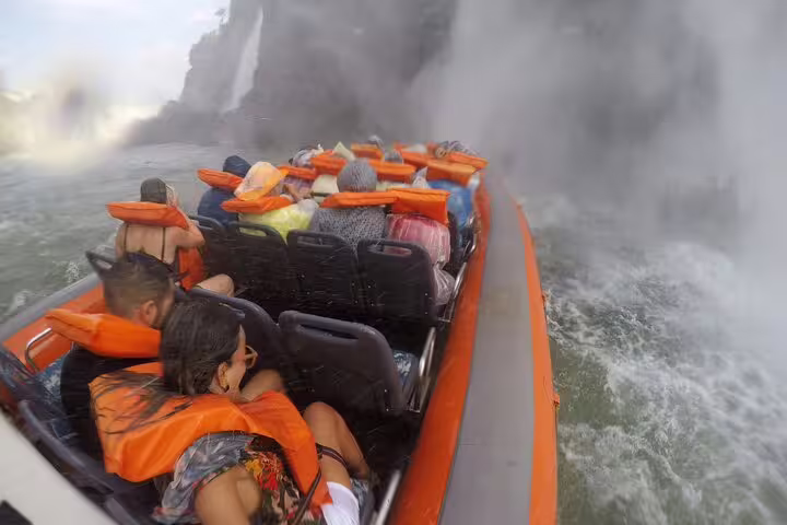 Tourists in a speedboat getting soaked near the breathtaking Foz do Iguaçu waterfalls, wearing bright orange life vests.