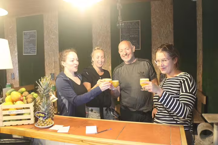 Group of tourists toasting with fresh drinks at a rustic bar, celebrating their adventure on the West volcanic pools tour.