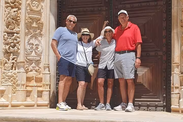 Four tourists pose happily in front of an ornately carved door in Tomar, showcasing local architectural beauty.