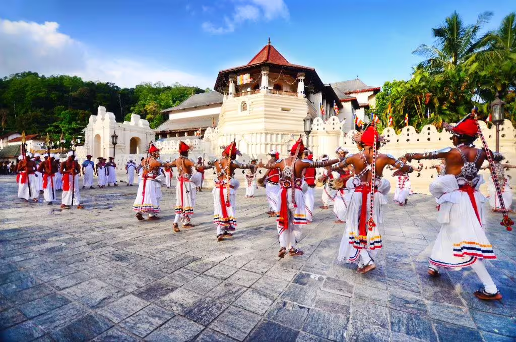 Traditional dancers in colorful attire performing outside a historic temple in Sri Lanka, capturing vibrant local culture.