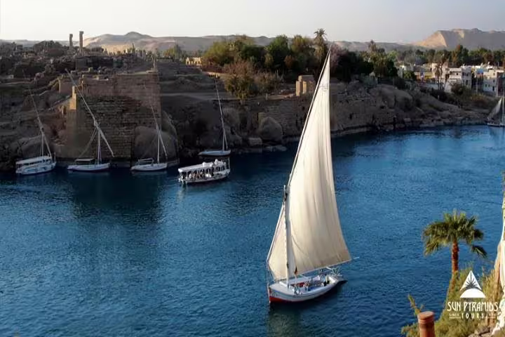 Traditional felucca sailing on the Nile in Aswan, Egypt, with riverbank ruins and islands in view