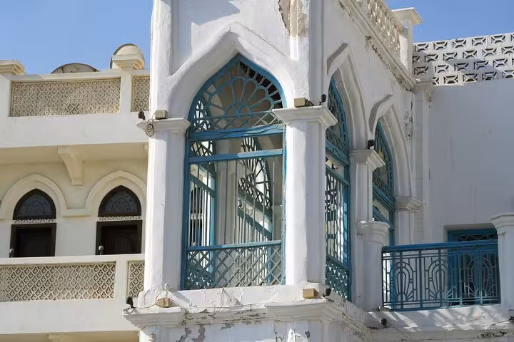 Close-up of traditional white Omani house with ornate blue arched windows seen on a cultural half-day Muscat city sightseeing tour