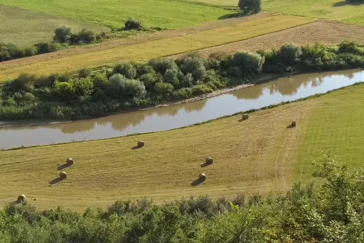 Aerial view of hay bales in a green Transylvania field beside a winding river