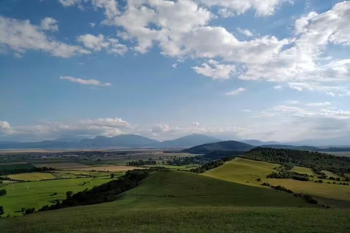 Green rolling hills and wide valley with mountains in the background on a Transylvania bike tour
