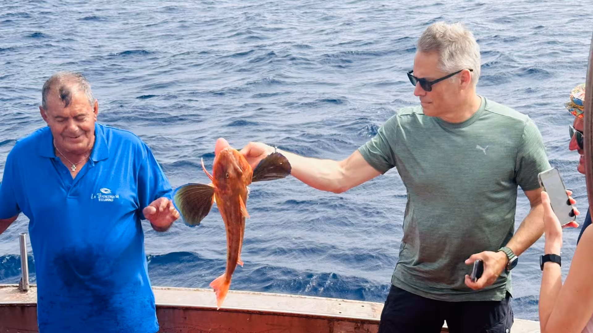 Guests holding a colorful fish on a fishing boat tour near the Egadi Islands from Trapani.