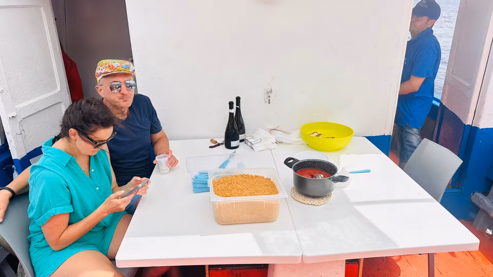Couple enjoying a meal on a fishing tour boat in the Egadi Islands, with local wine and snacks on the table.