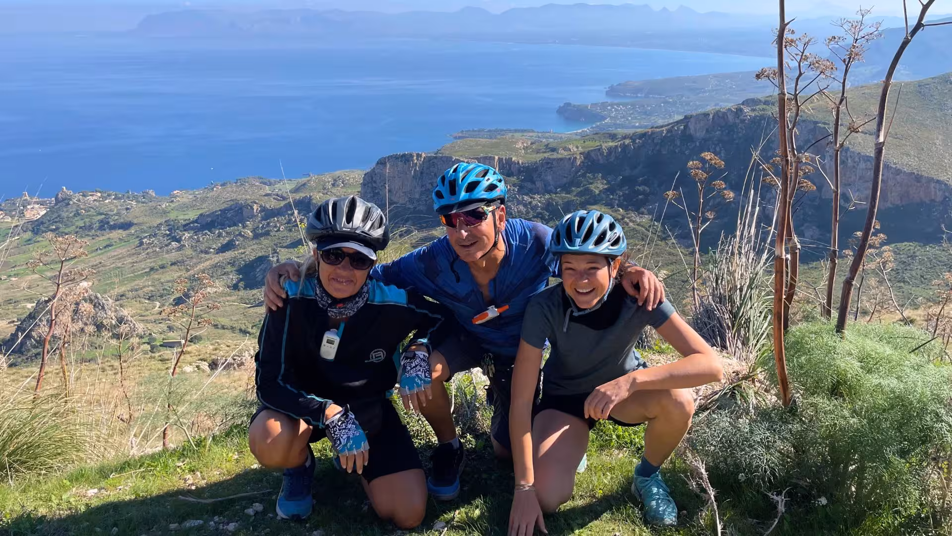 Friends pose with helmets, smiling against Erice's stunning ocean backdrop on an exciting e-bike tour from Trapani.