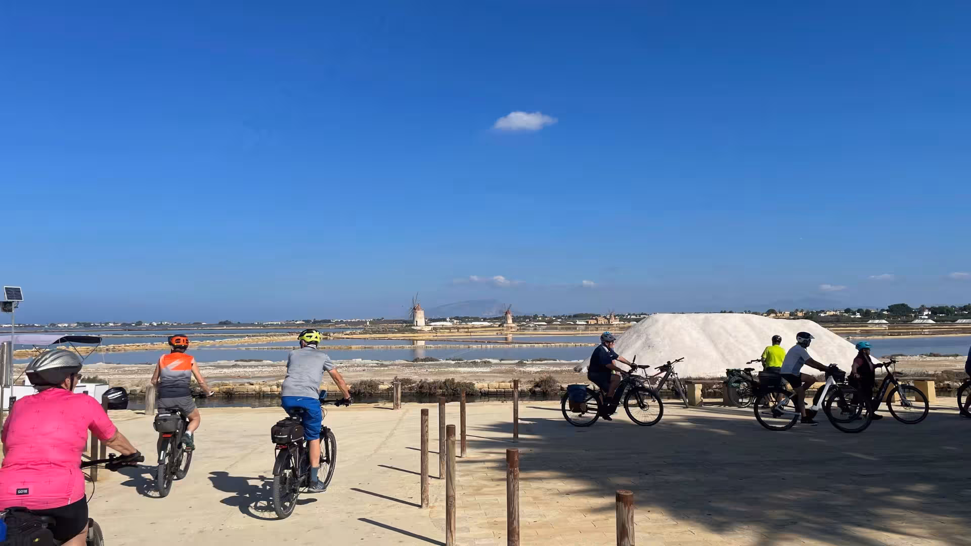 Cyclists enjoy an e-bike tour through the scenic salt pans of Trapani to Marsala, with windmills in the background.