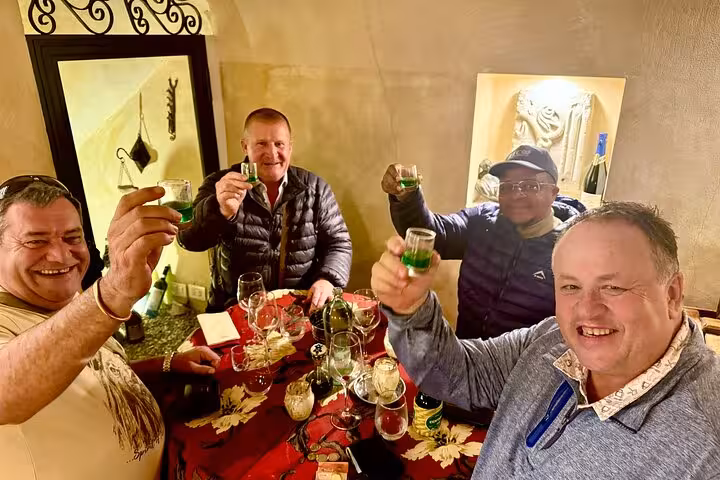 Happy small group raising green liqueur shots during a Trastevere food and wine tasting evening in Rome, Italy
