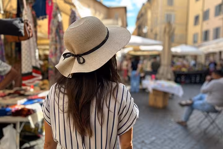Woman in a sun hat exploring a vibrant market street in Trastevere, Rome, during a food and wine tour.