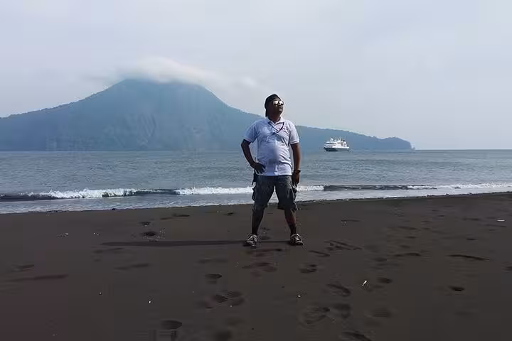 Traveler on black sand beach with Anak Krakatau volcano views, Krakatoa day tour from Lampung by boat