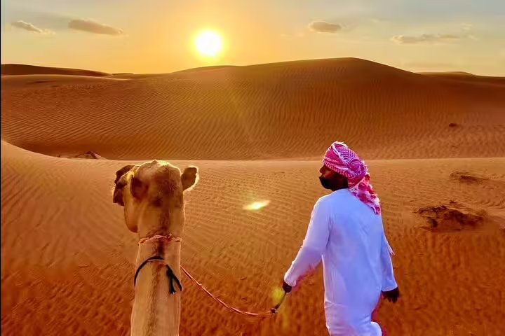 Traveler leads camel through serene desert at sunset during private full-day tour, capturing breathtaking views.