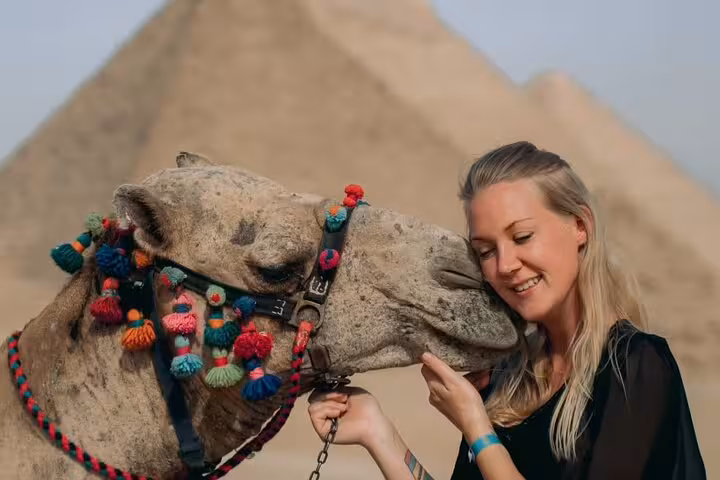 Traveler cuddling a decorated camel at Giza Pyramids on a 3-day Cairo tour with museum and hostel stay