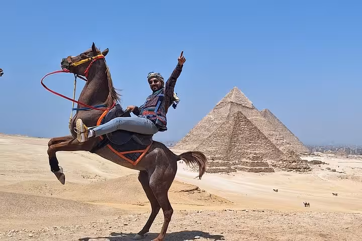 Traveler on horseback poses triumphantly near the iconic Pyramids of Giza, showcasing adventure in Egypt.