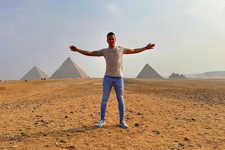 Traveler posing on Giza Plateau with pyramids behind, Cairo luxury day tour combining Memphis, Saqqara and Dahshur