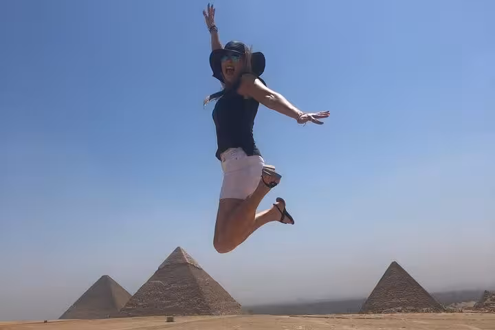 Traveler jumping with Giza pyramids backdrop on private Giza and Sphinx tour in Cairo, including camel ride and lunch