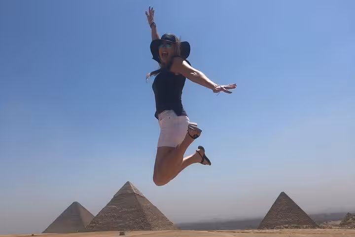 Traveler jumping with Giza Pyramids behind on a private tour, panoramic desert views under blue sky