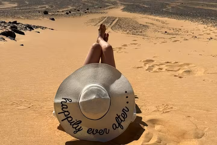 Traveler relaxing on golden dunes in Egypt, part of private two-day Black and White Desert camping experience