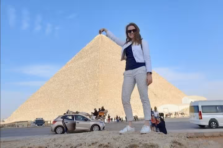 Traveler posing with the Great Pyramid of Giza on a full-day tour with pickup, visiting Giza, Saqqara and Memphis