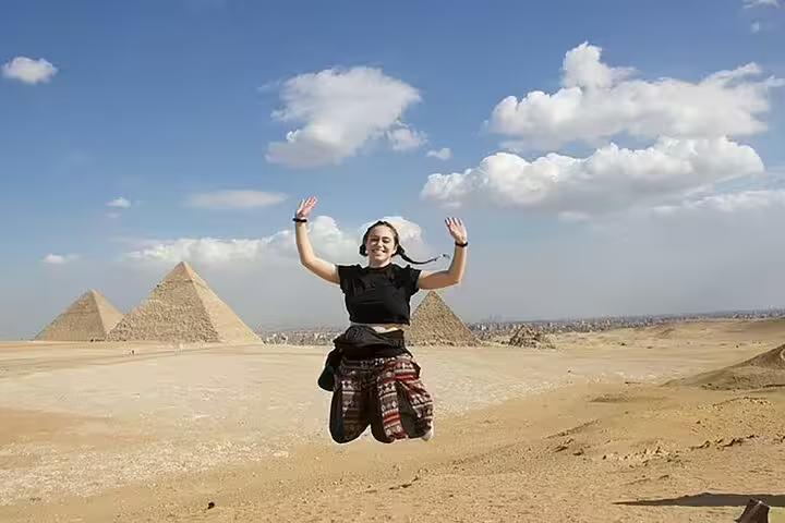 Traveler jumping with Giza Pyramids backdrop on private Alexandria port day tour, Egypt shore excursion