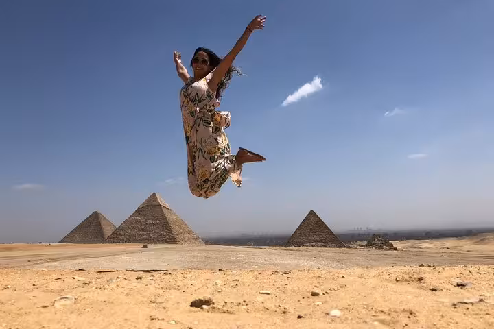 Traveler jumping at Giza Plateau with pyramids in background on a private tour to Giza Pyramids and desert views