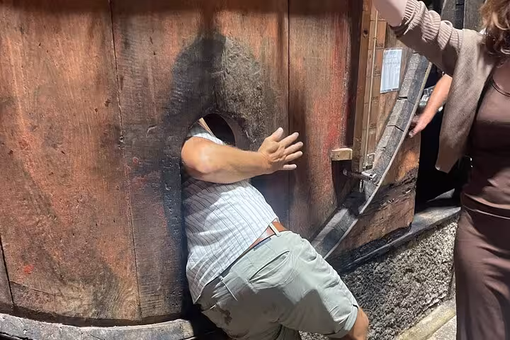 Traveler entering a giant oak wine barrel at a Douro Valley winery on a Porto tour with sommelier and boat trip