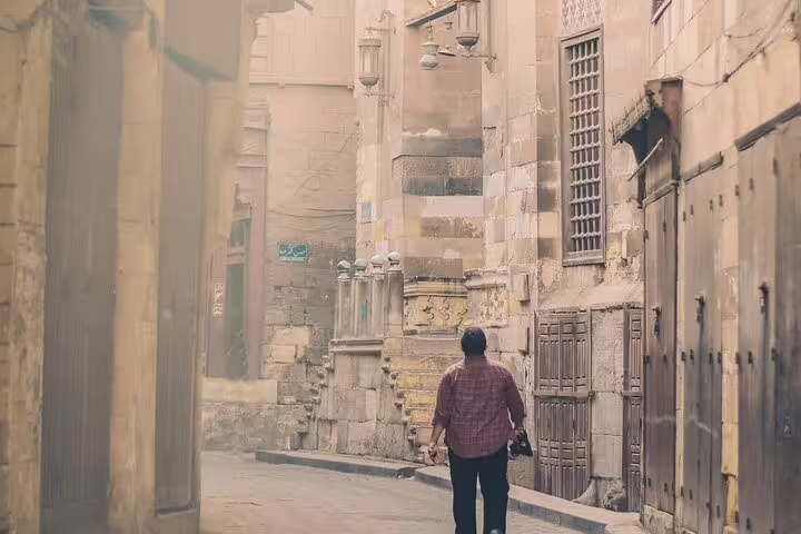 Traveler walking Old Cairo alley with historic stone buildings, cultural stop on Citadel and bazaar day tour