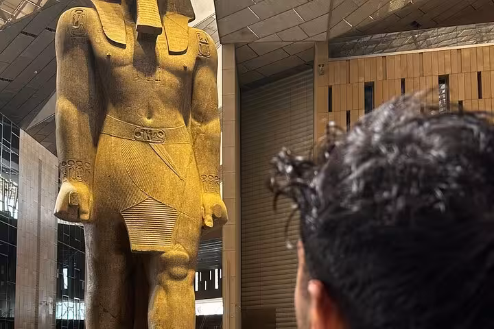 Traveler viewing colossal ancient pharaoh statue inside Grand Egyptian Museum on Giza pyramids tour with lunch