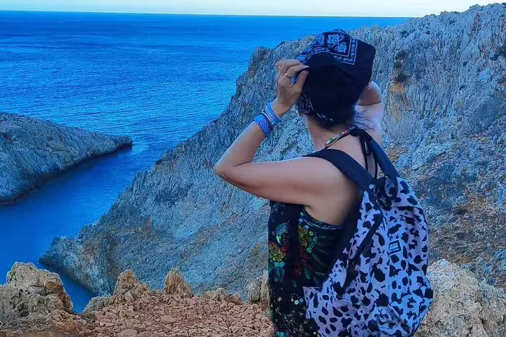 Traveler with a backpack admiring the stunning cliffside view of Seitan Limania's turquoise waters.